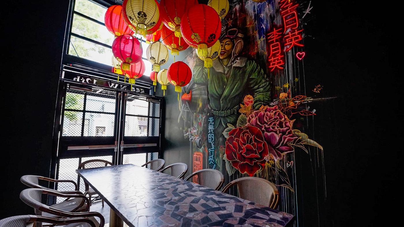 The Hazel Ying Room at The Malarkey, with red lanterns over a communal table and a mural of pilot Hazel Ying Lee